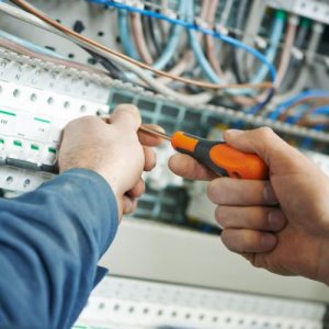 2 Hände eines Elektrikers, die gerade etwas in einem Schaltschrank einbauen.
